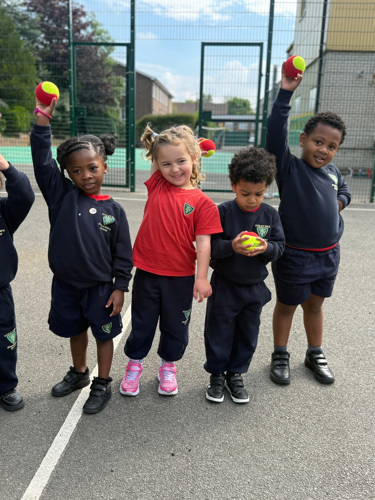 Children at Little Vita’s Nursery on the outdoor play area, holding tennis balls high